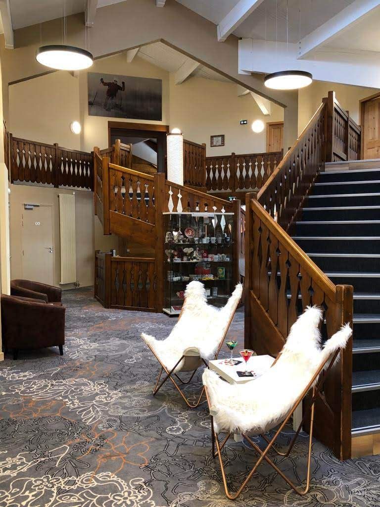 En rummelig lobby med en imponerende trappe, en reception og et siddeområde med hvide pelsstole.