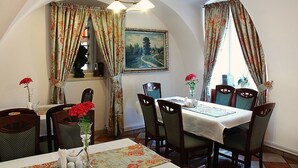 A dining area with a table set for four, surrounded by chairs, a painting on the wall, and floral curtains. - Hotel Przy Oślej Bramie - Zamek Książ (Walbrzych)