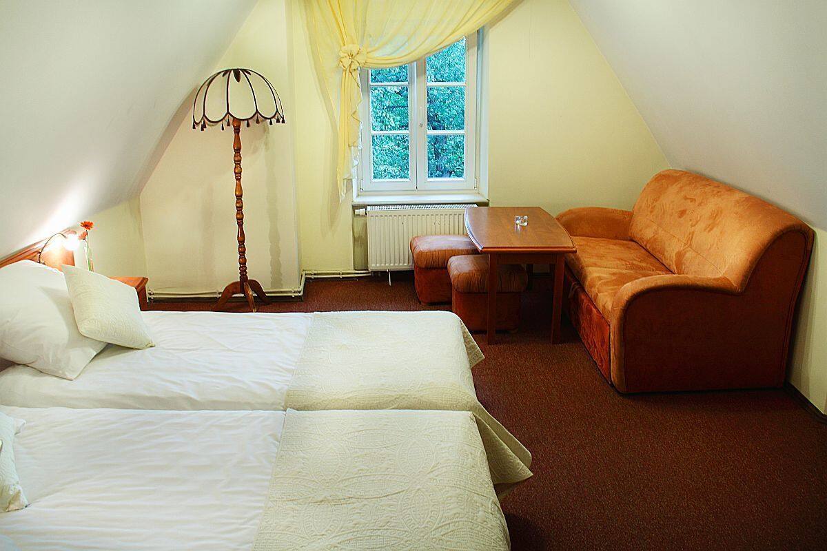 A bedroom with a bed, a sofa, a table, and a window with curtains.