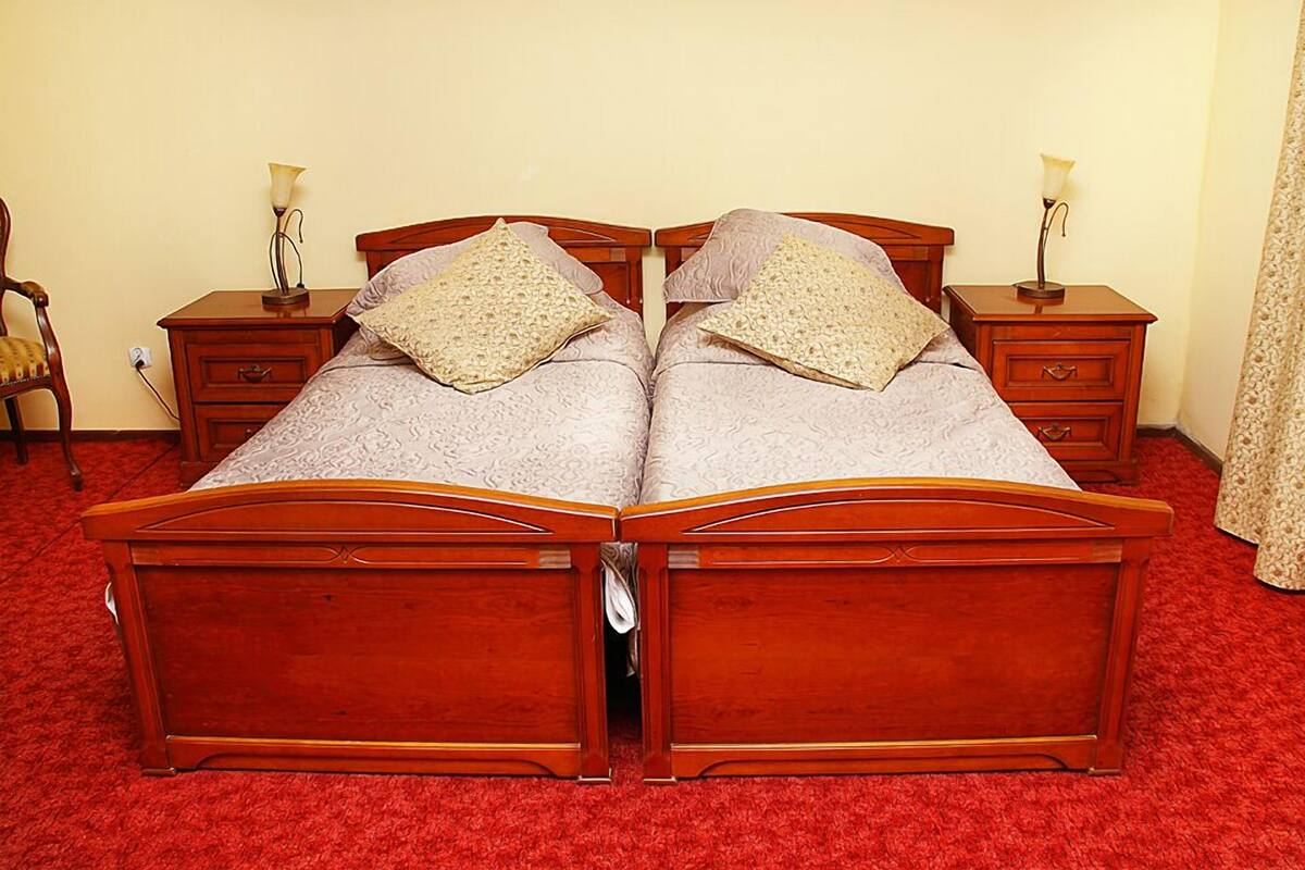 A double bed with a wooden frame, two bedside tables with lamps, a chair, and a red carpeted floor.