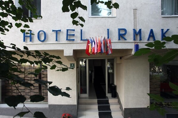 A hotel entrance with the name "HOTEL IRMAK" above the door. There are flags hanging on the wall and a staircase leading to the entrance. - Hotel Irmak (Sarajevo)