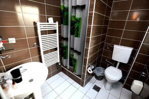 A modern bathroom with a white sink, toilet, and shower curtain with a green leaf pattern. - Hotel Irmak (Sarajevo)