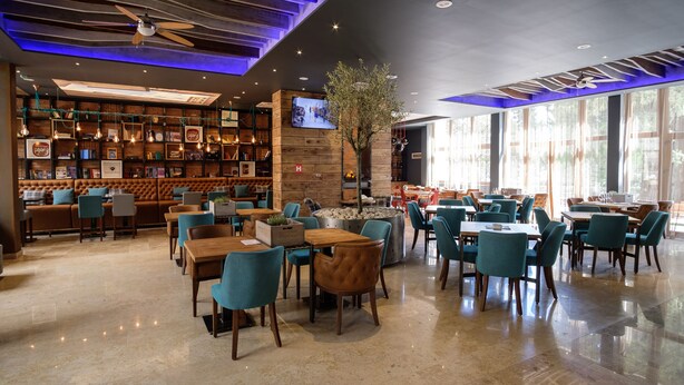 Un restaurant moderne doté d’un bar, de différents types de tables et de chaises, ainsi que d’une grande fenêtre laissant entrer la lumière naturelle.