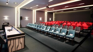 Une salle de conférence avec des rangées de chaises, un pupitre et un écran de projection.
