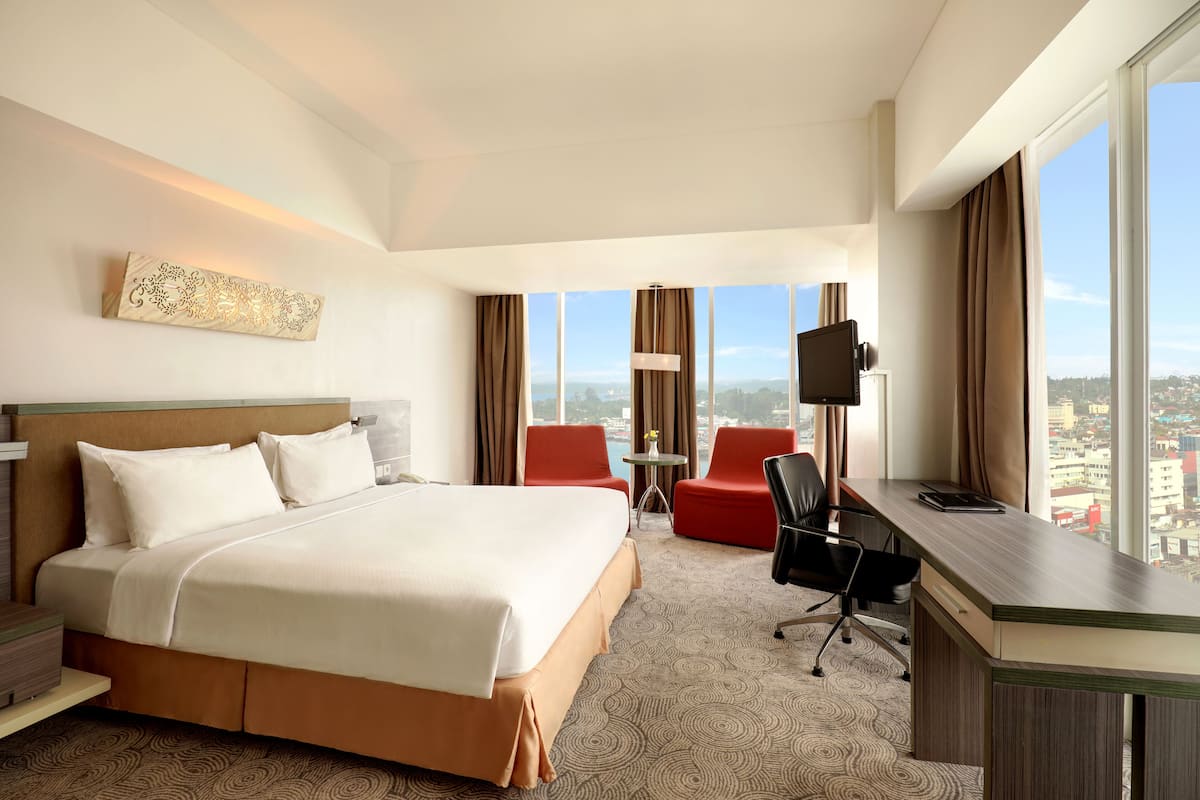Een hotelkamer met een groot bed, een bureau, twee stoelen, een televisie en uitzicht op de stad.