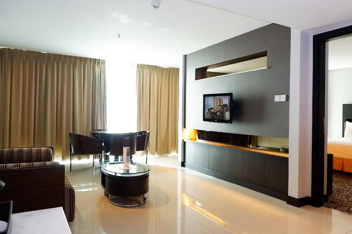 Een moderne hotelkamer met een flatscreen televisie aan de muur, een sofa, een rond bijzettafeltje en een bed met hoofdeinde.