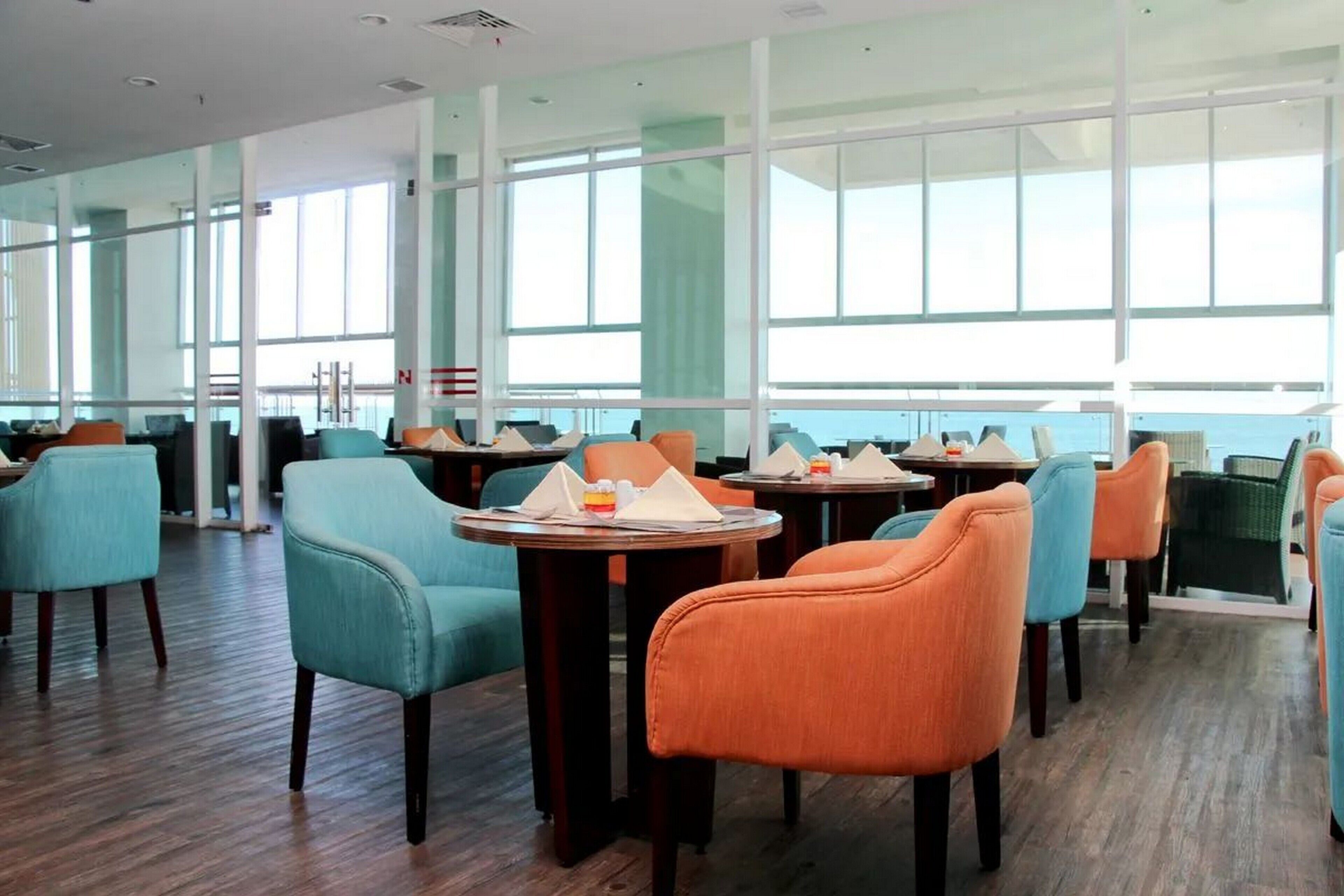 A modern dining area with round tables and chairs, large windows, and a wooden floor.