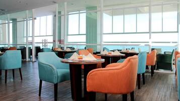 A modern dining area with round tables and chairs, large windows, and a wooden floor.