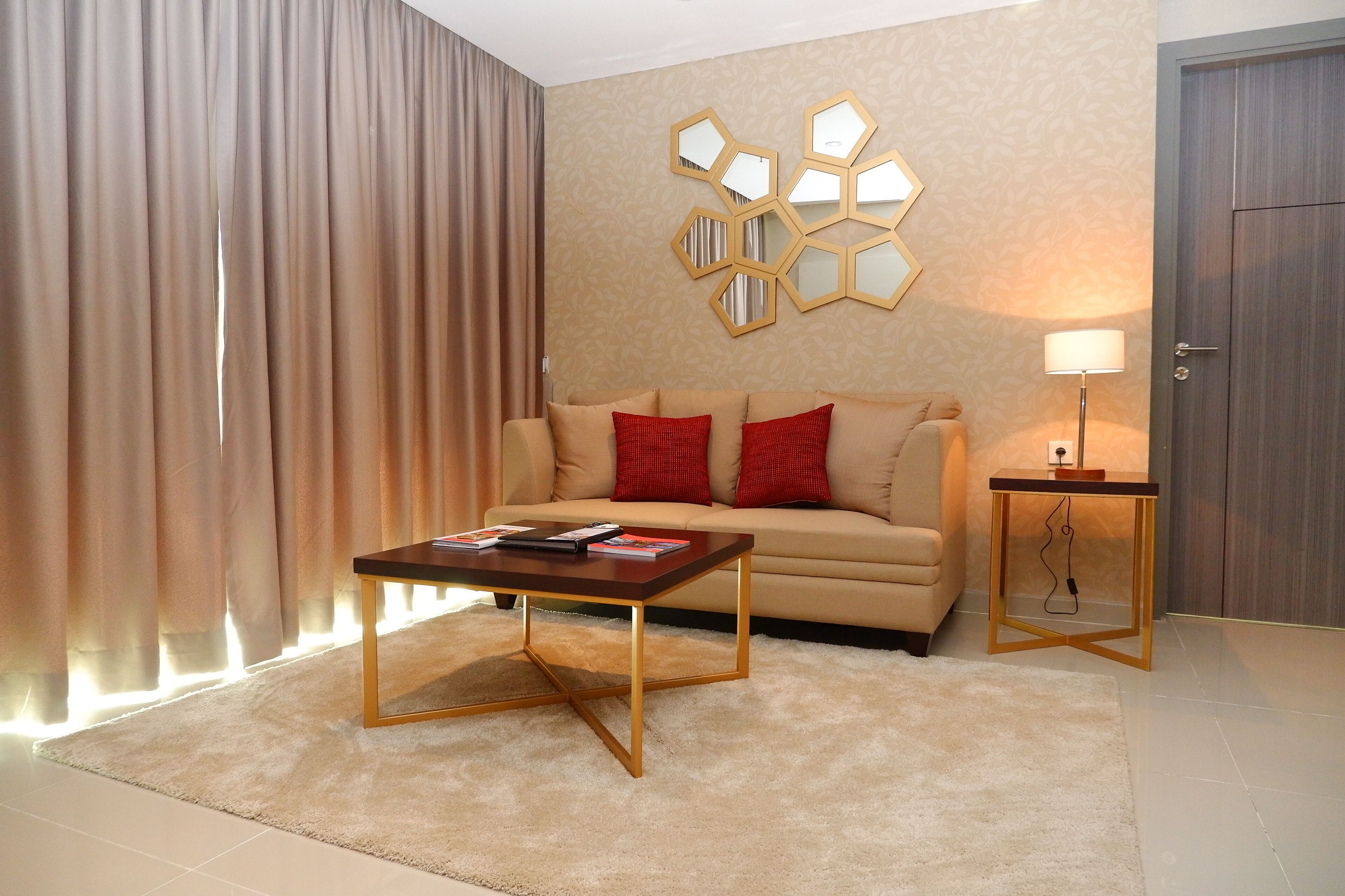 Un salon comprenant un canapé, une table basse, une lampe et un mur orné de miroirs hexagonaux.