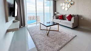 Ein modernes Wohnzimmer mit großem Fenster und Meerblick, einer Couch mit roten Kissen und einem Couchtisch.