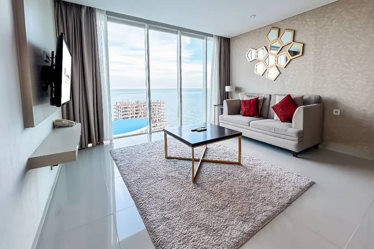 Een moderne woonkamer met een groot raam met uitzicht op zee, een bank met rode kussens en een salontafel.
