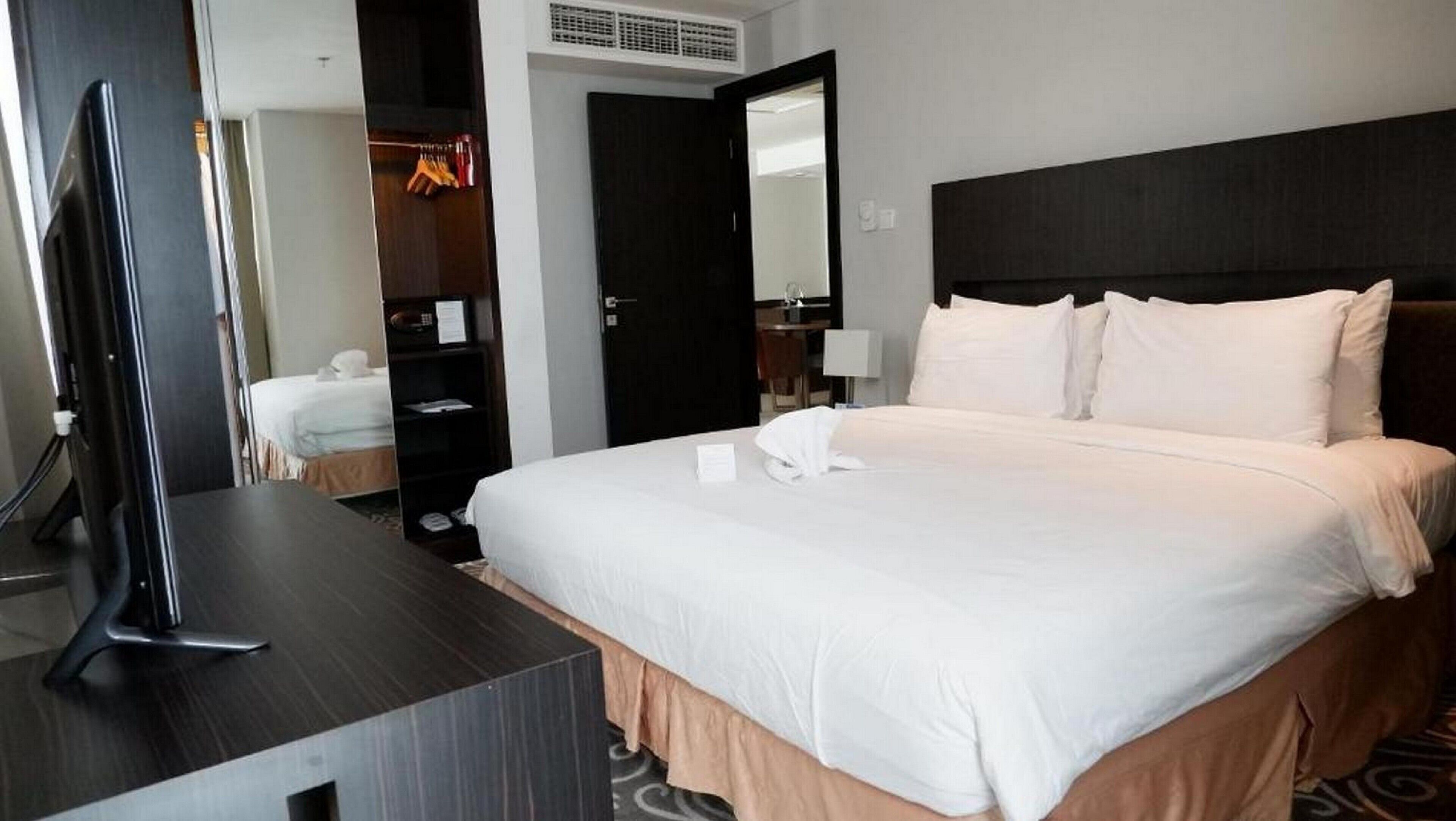 A hotel room with a large bed, a TV on a stand, a wardrobe, and a mirror.