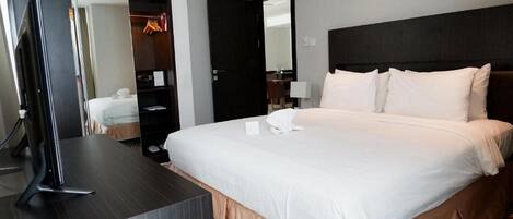 A hotel room with a large bed, a TV on a stand, a wardrobe, and a mirror.