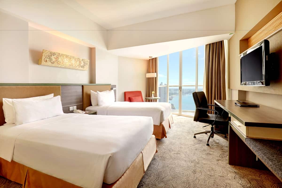 Een hotelkamer met twee bedden, een bureau, een stoel, een televisie en een groot raam met uitzicht over de stad.