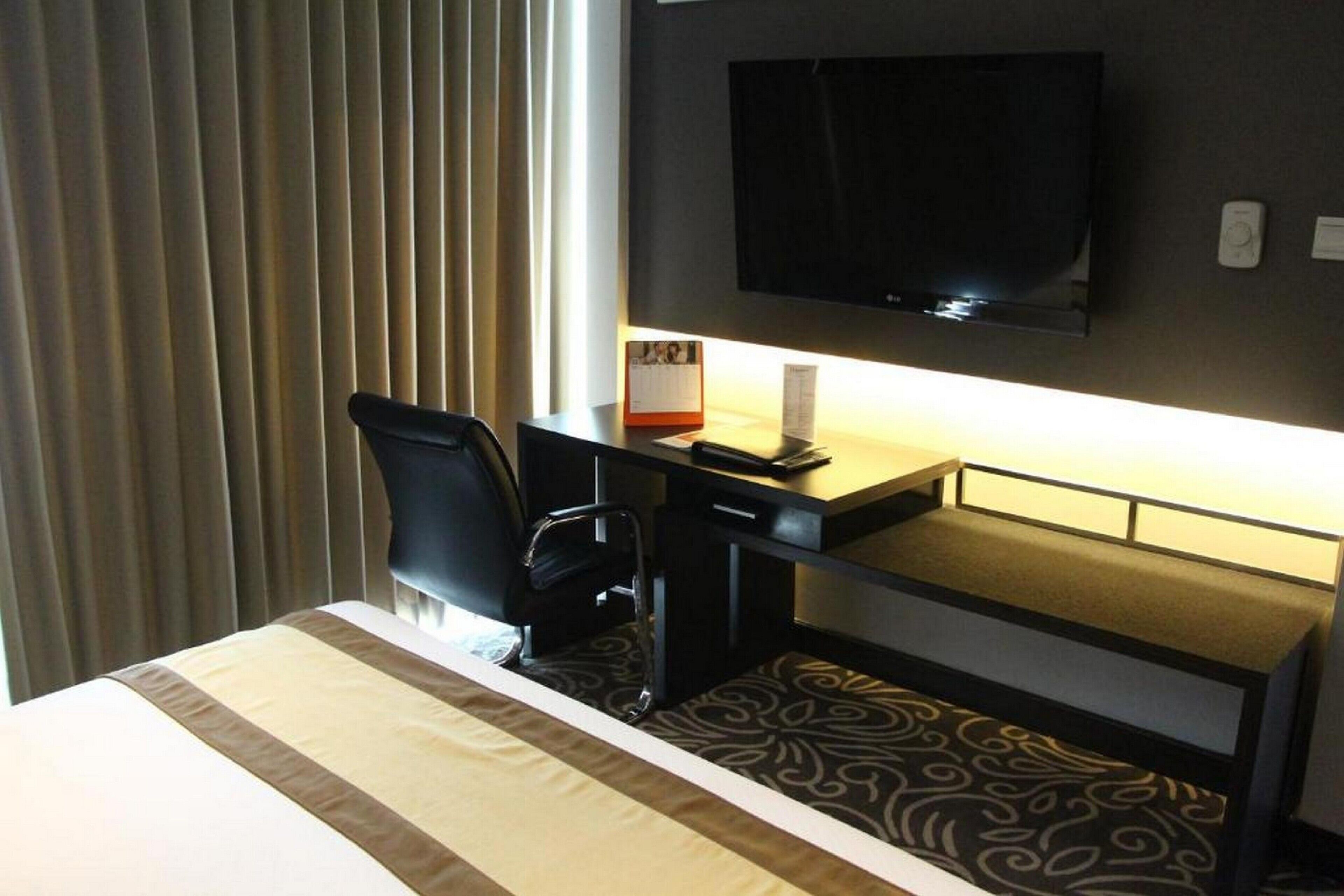 Hotelkamer met een bed, een bureau met stoel, een flatscreen televisie aan de muur en een raam met gordijnen.