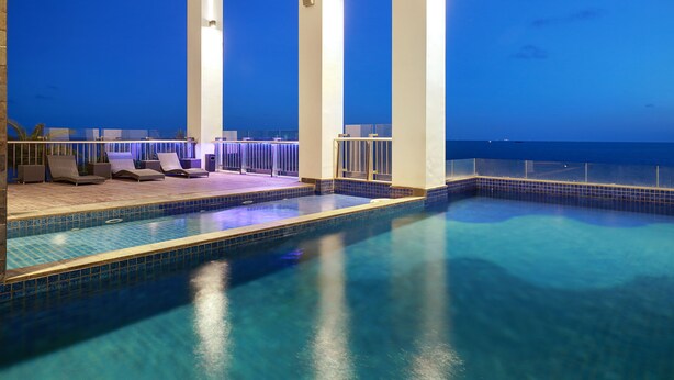 Ein Poolbereich mit Liegestühlen und Blick aufs Meer im Abendlicht.