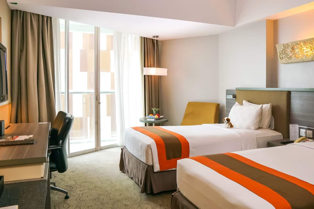 Een hotelkamer met twee bedden, een bureau, een stoel, een klein tafeltje met fruit en een wandlamp.