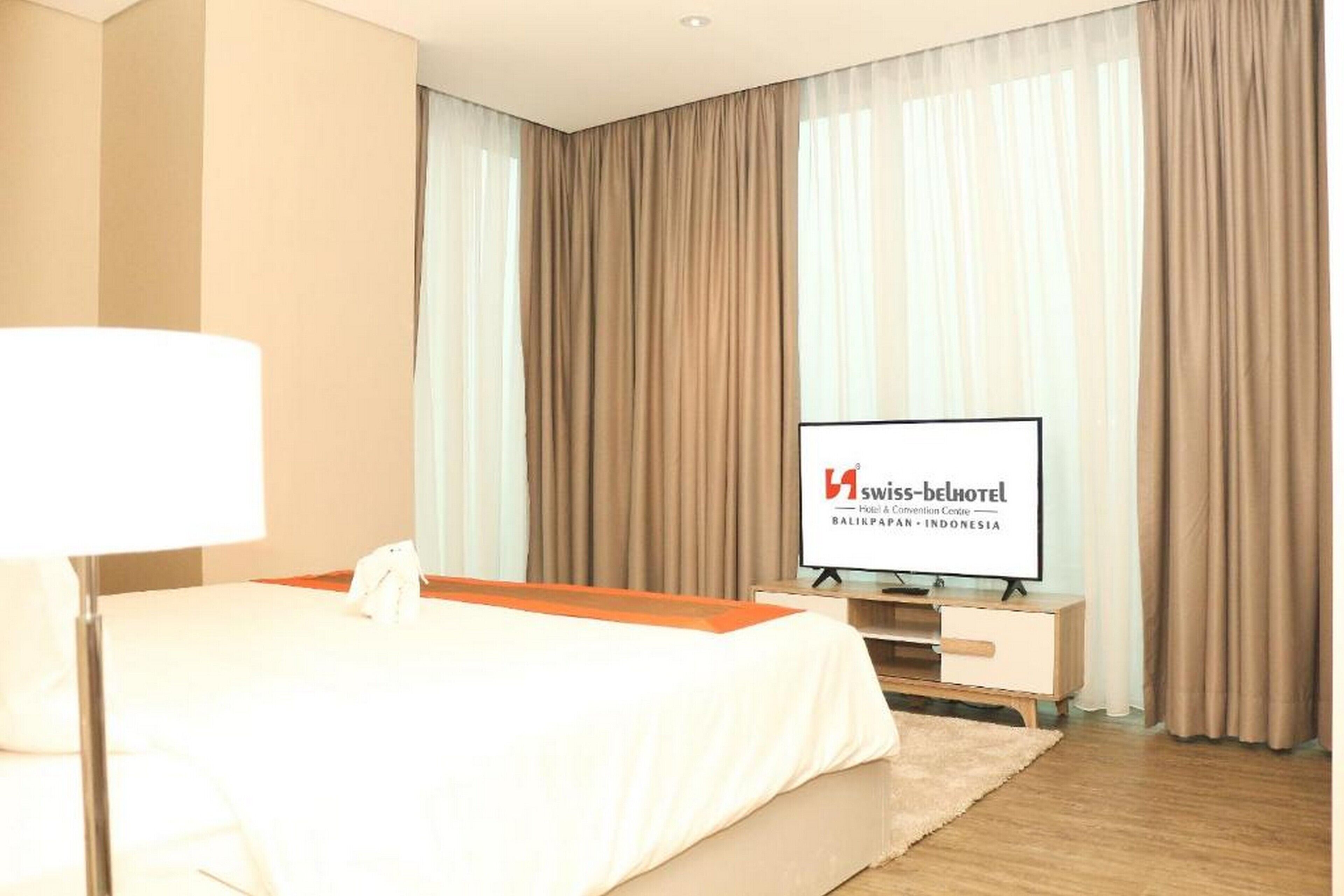 A hotel room with a bed, a TV, and curtains.