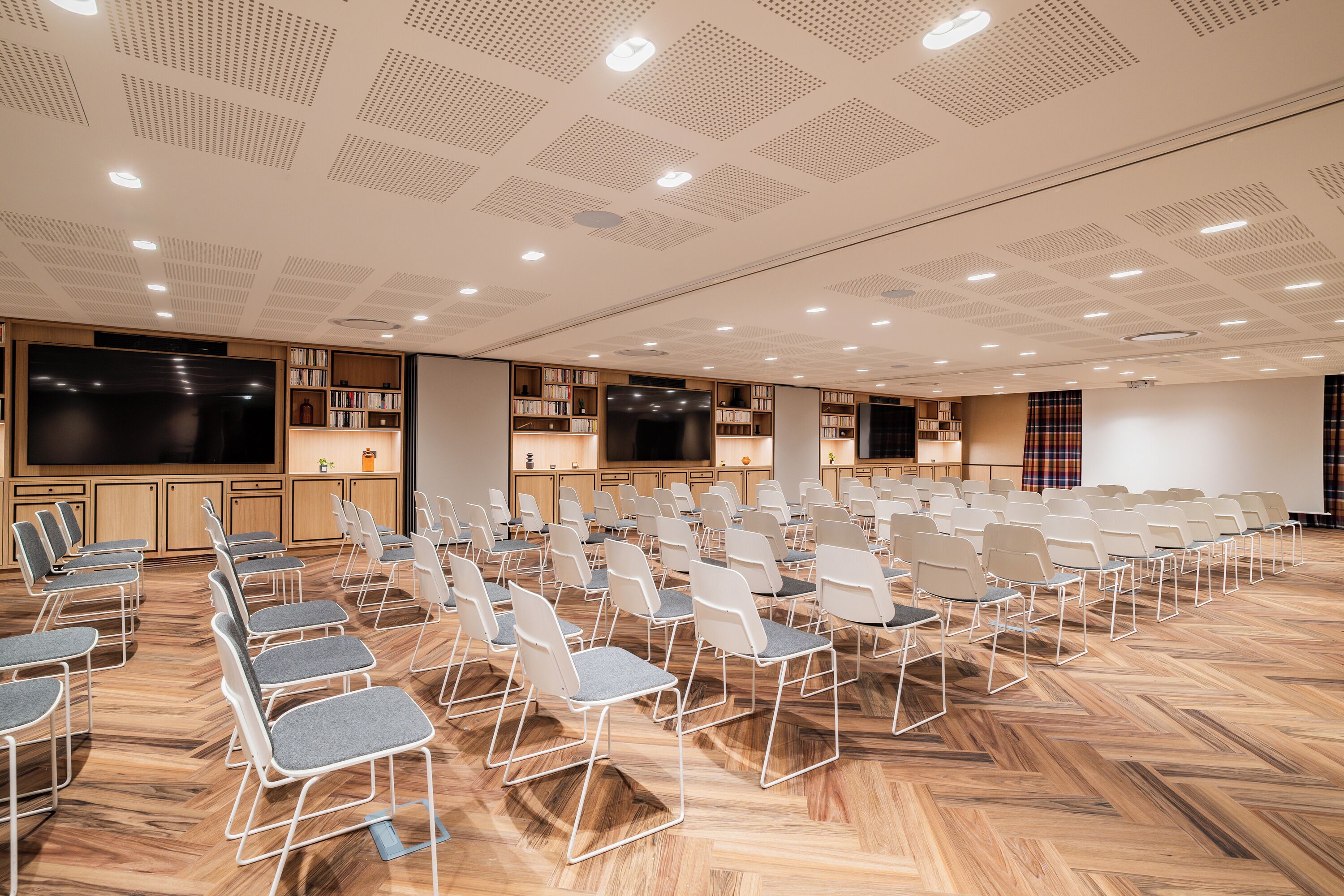 Een vergaderzaal met rijen stoelen, een groot scherm en boekenkasten.