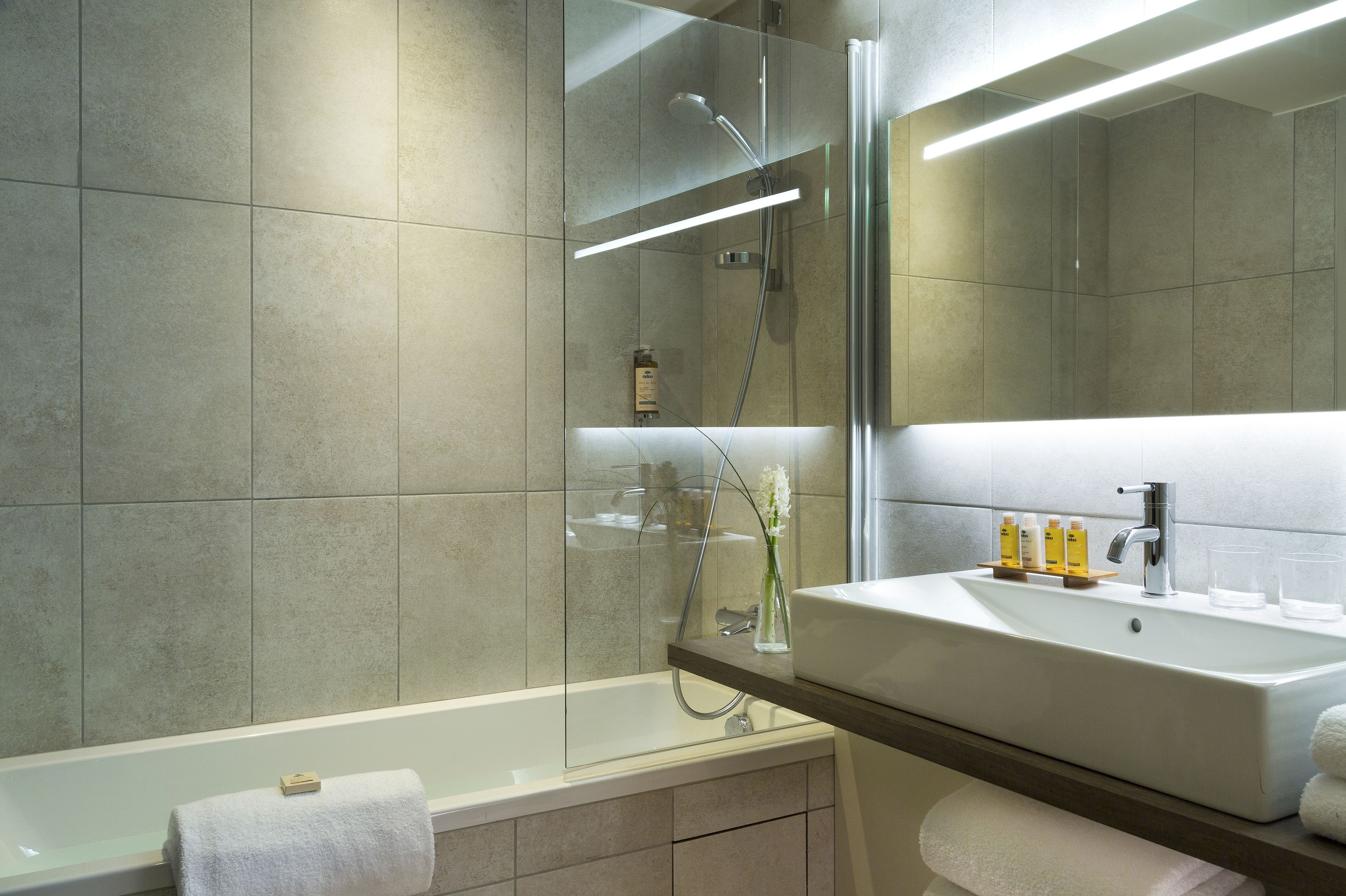 Un baño moderno con bañera, ducha con mampara de vidrio y tocador con espejo.
