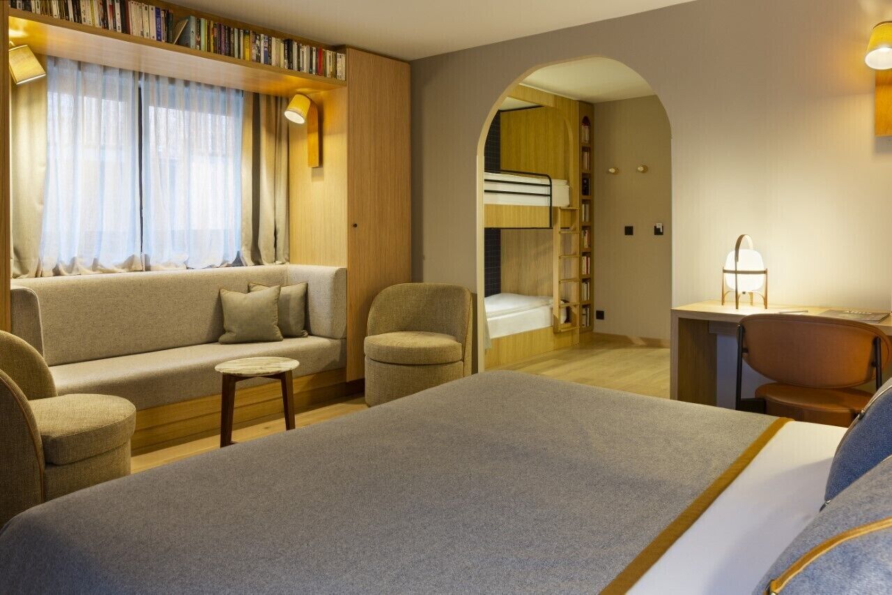A hotel room with a sofa, armchairs, a desk, a bunk bed, and a bookshelf.