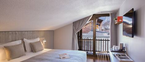 A bedroom with a large bed, a desk with a chair, a TV, and a window with a view of a mountain.