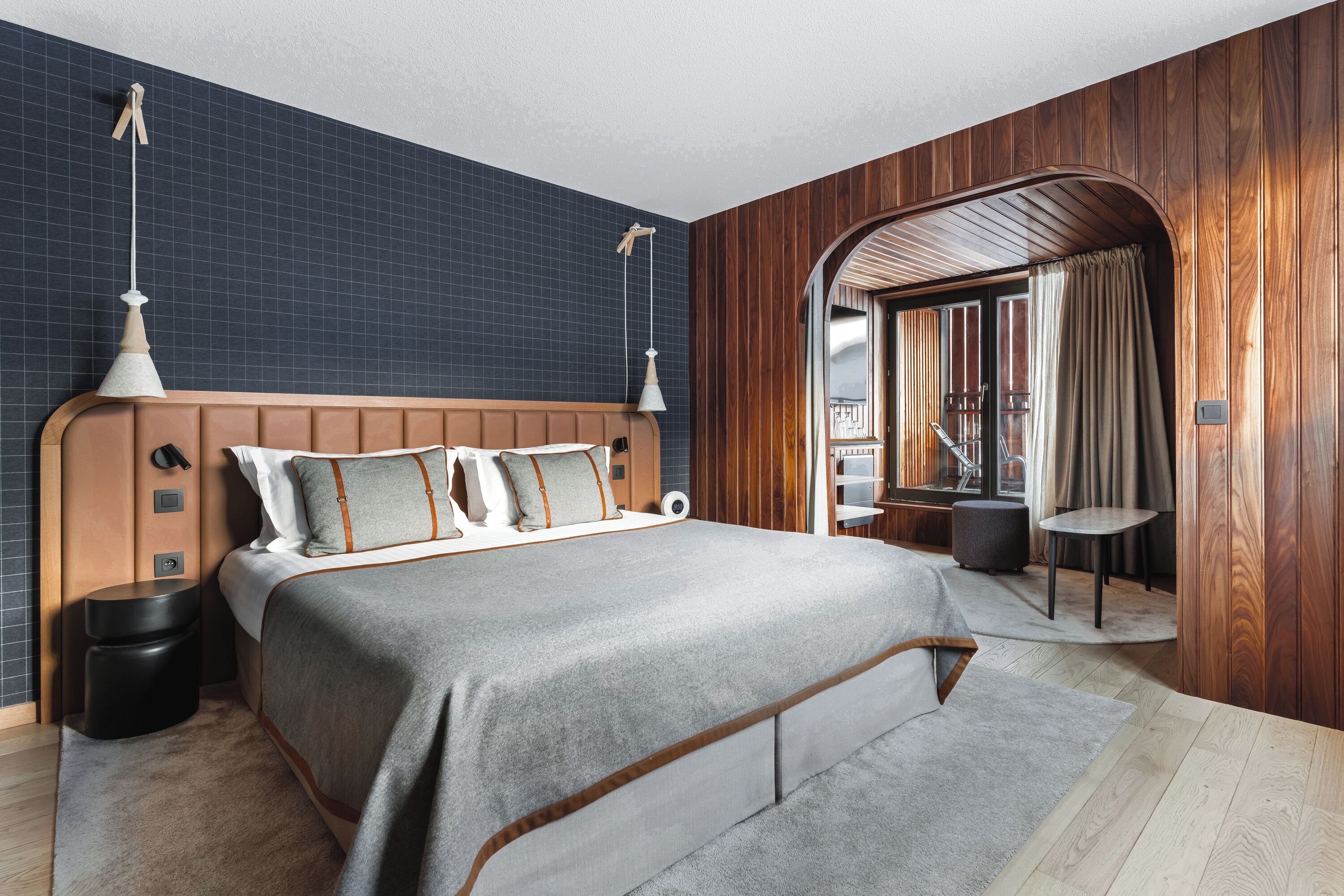A modern bedroom with a large bed, wooden paneling, and a view through an arched doorway.