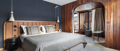 A modern bedroom with a large bed, wooden paneling, and a view through an arched doorway.