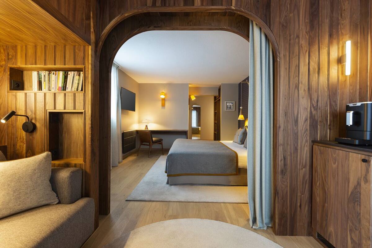 A cozy hotel room with a wooden interior, a bed, a desk, and a bookshelf.