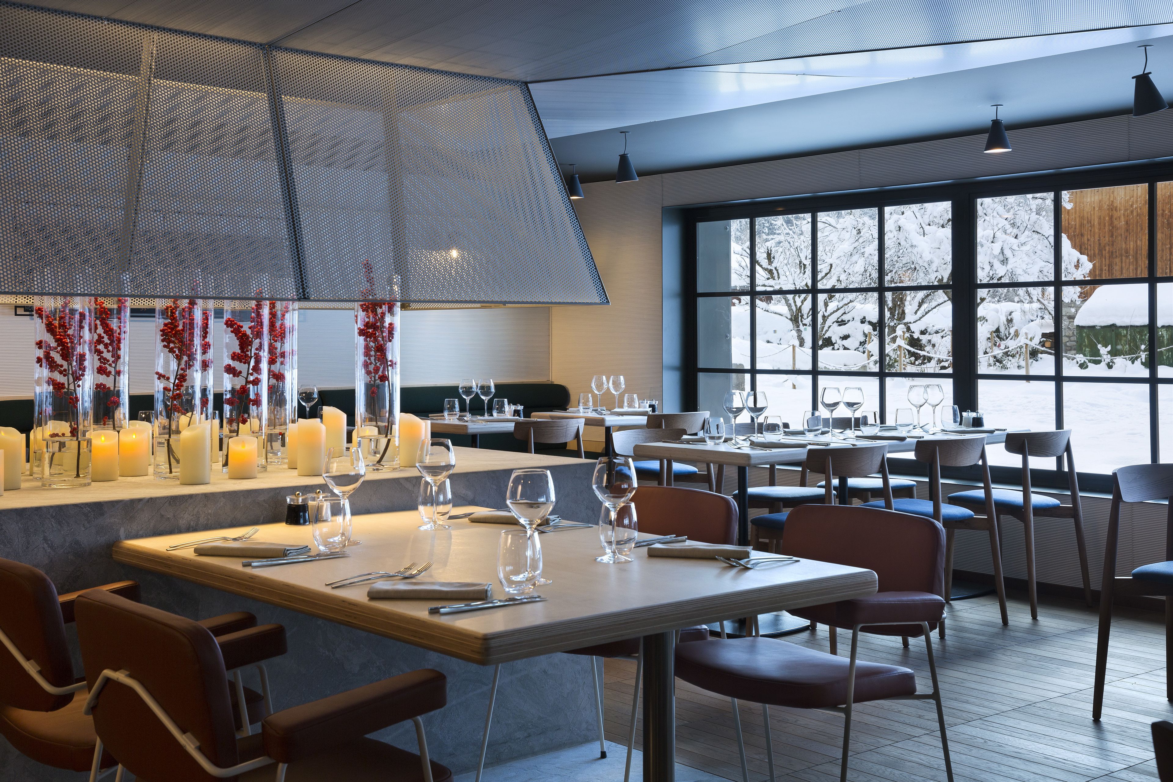 Un interior de restaurante moderno con mesas dispuestas para comer, un ventanal con vistas a árboles cubiertos de nieve y un techo decorativo.