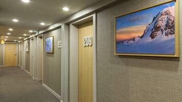 Een hotelgang met deuren genummerd 201 en 209, bekleed met tapijt, en kunstwerken in lijsten aan de muren.
