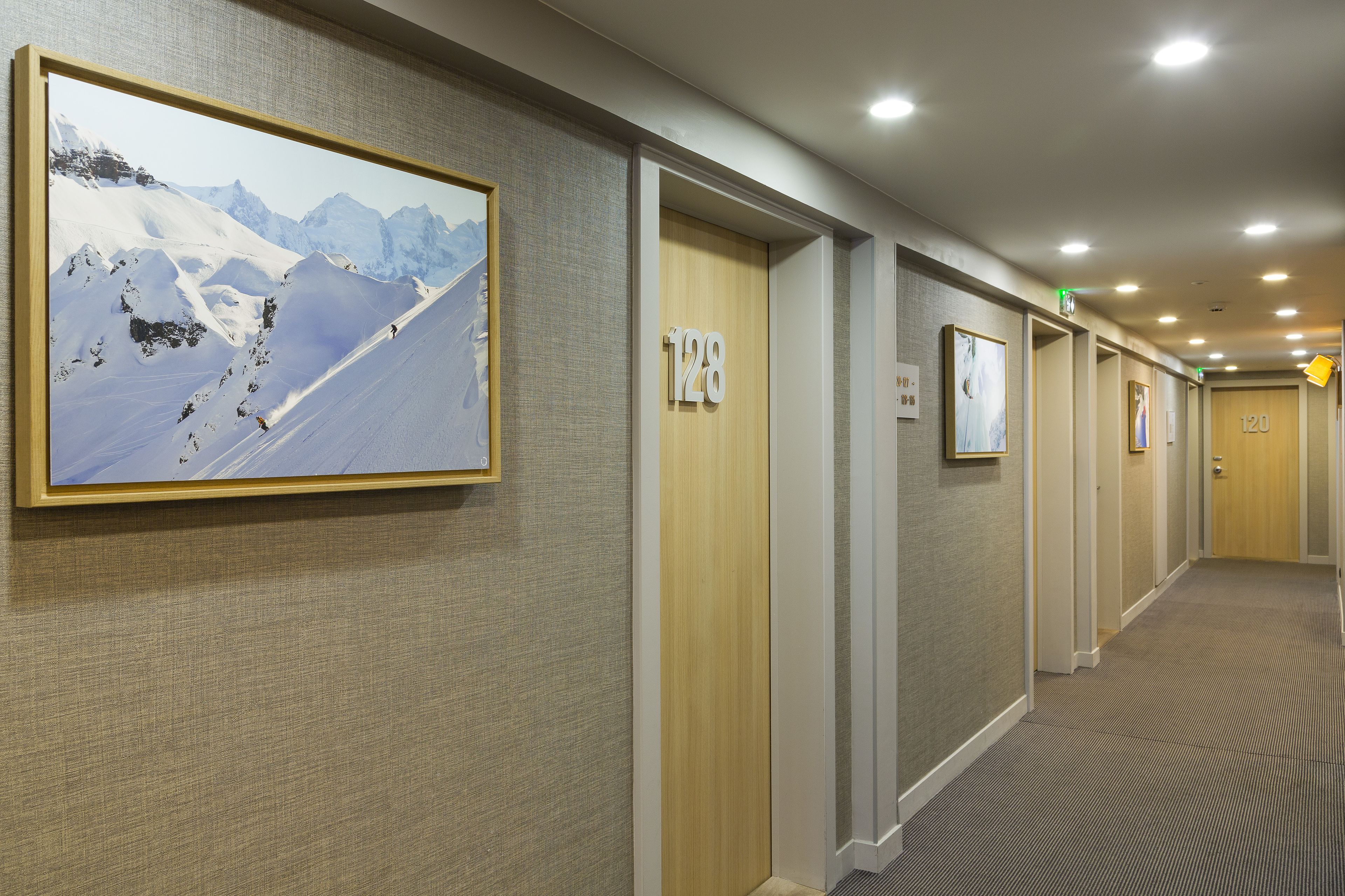 A hotel hallway with framed artwork, numbered doors, and a carpeted floor.