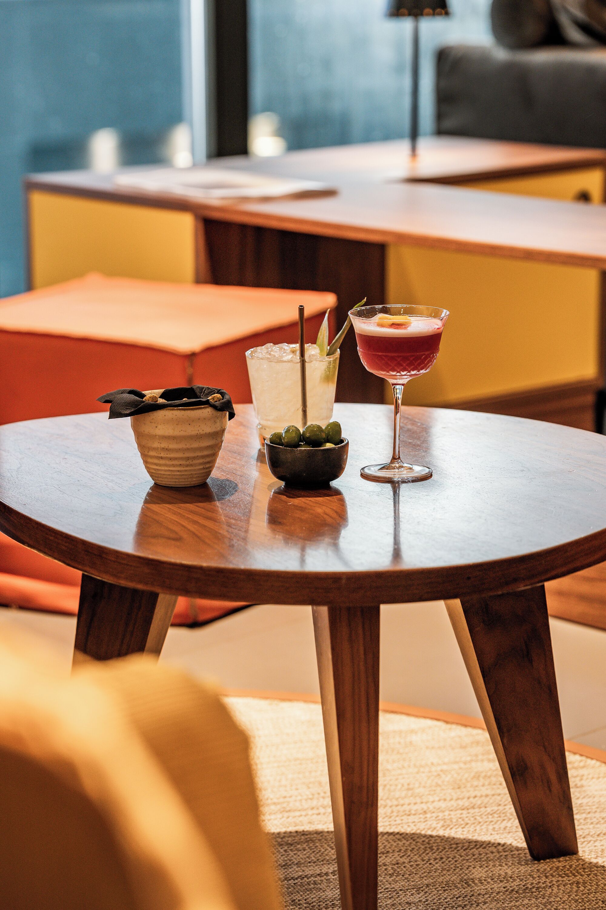A round wooden table with a bowl, a glass with a drink, and a martini glass with a garnish.