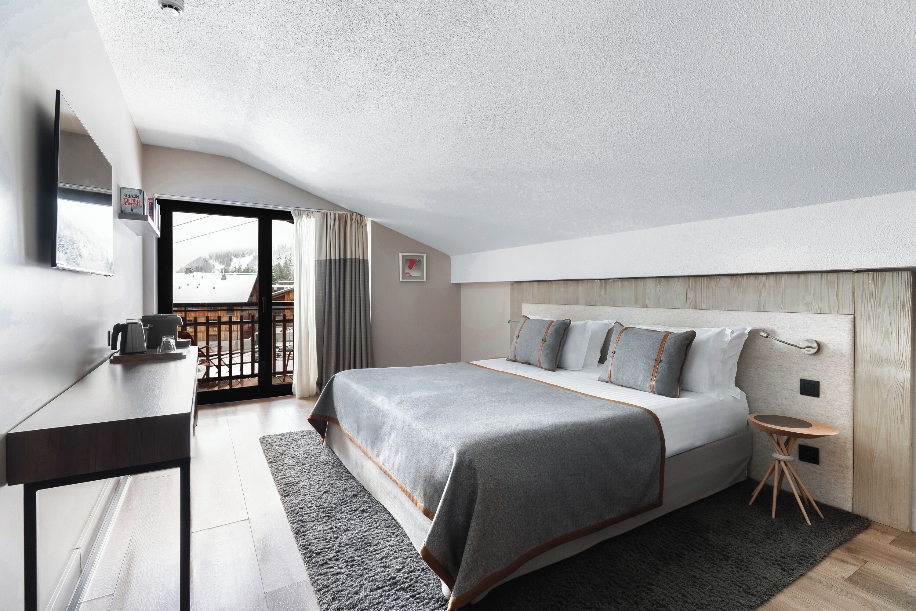 Habitación de hotel moderna con una cama grande, un escritorio y vistas a un paisaje nevado desde el balcón.
