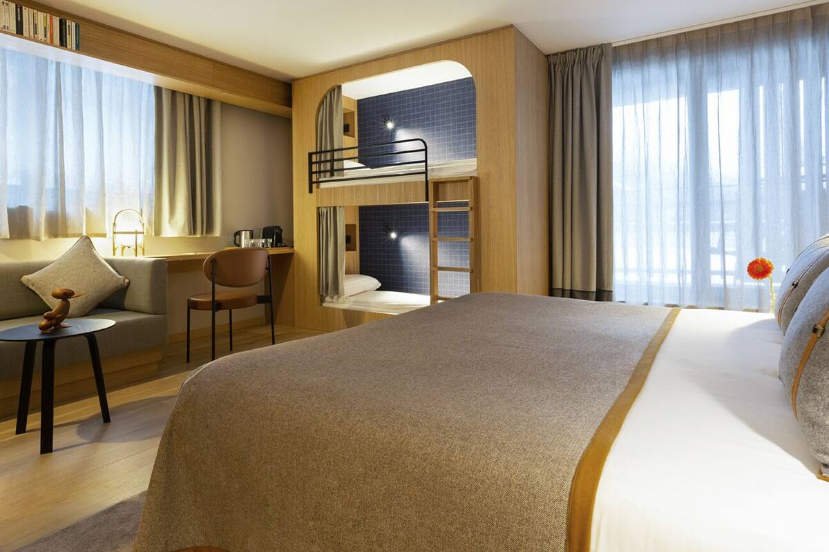 A hotel room with a bunk bed, a desk, a chair, a sofa, and a small table.