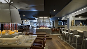 A modern restaurant with a central bar area, multiple seating options including bar stools and tables, and a contemporary interior design.