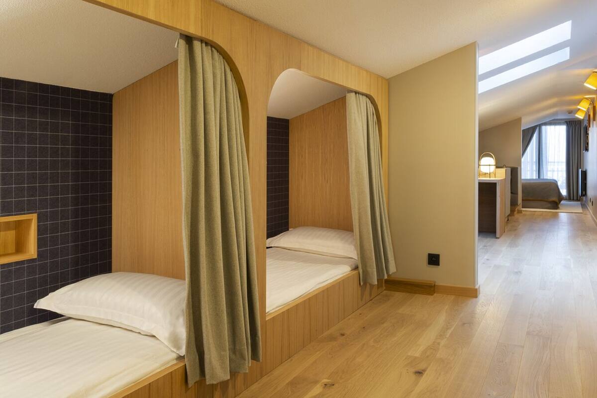 A hotel room with three wooden bunk beds, a small desk with a chair, and a view of the corridor.