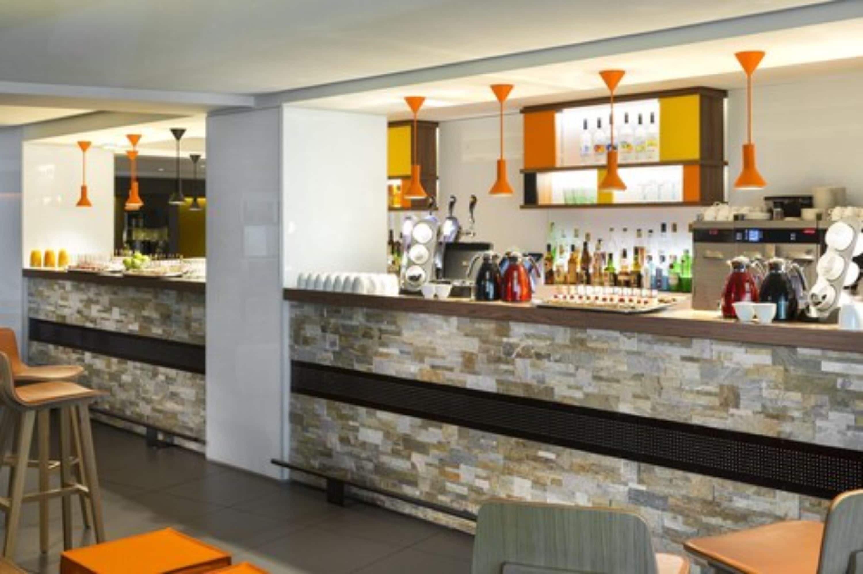 A modern bar area with a stone counter, orange pendant lights, and a variety of bottles and glasses.
