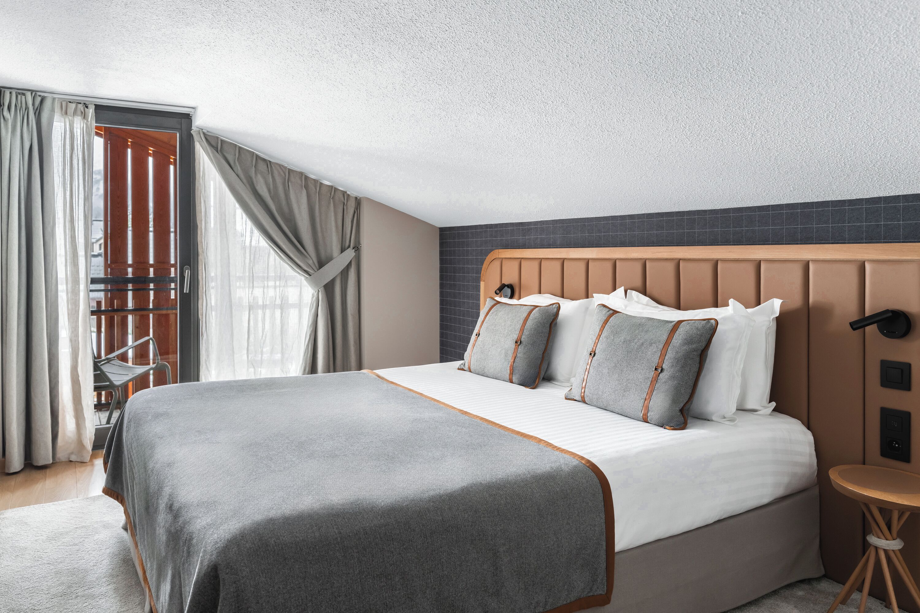 Een moderne hotelkamer met een groot bed, een houten hoofdeinde en een klein rond tafeltje.