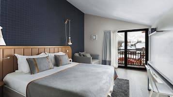 Ein modernes Hotelzimmer mit einem großen Bett, einem Fernseher, einem Balkon mit Bergblick und einer dunkelblauen Akzentwand.