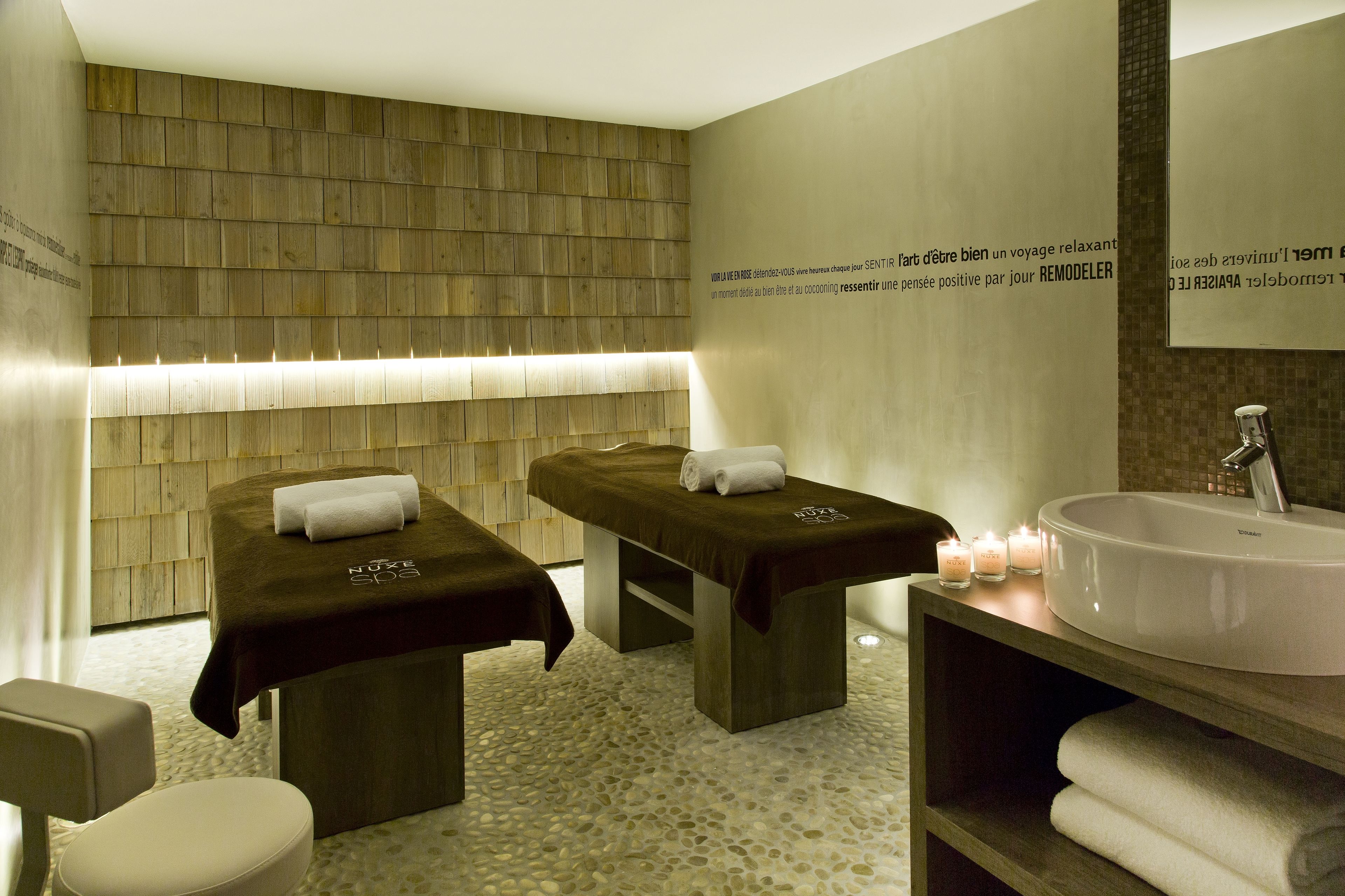 Une salle de spa équipée de deux tables de massage, d’un grand lavabo et de bougies.