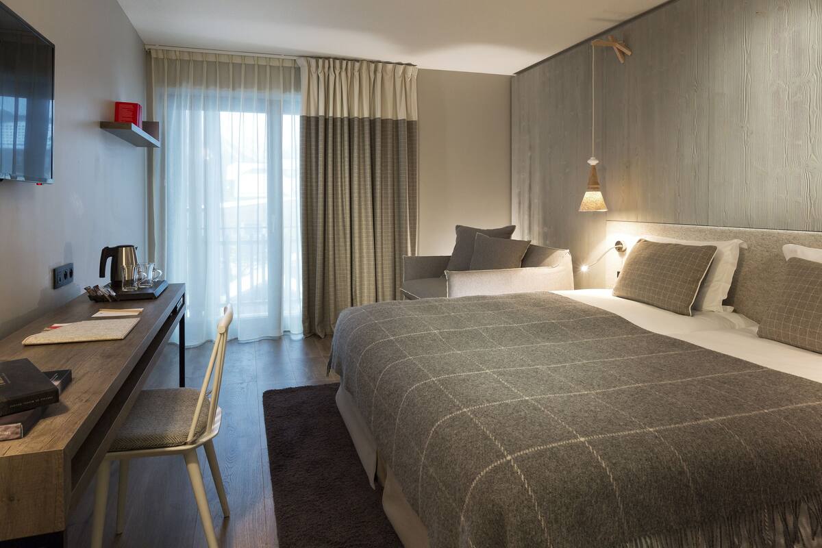 A hotel room with a large bed, a desk with a chair, a television, and a window with curtains.