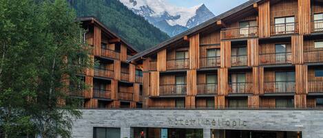 Ein Hotel mit einer steinernen Fassade, hölzernen Balkonen und einer Bergkulisse.