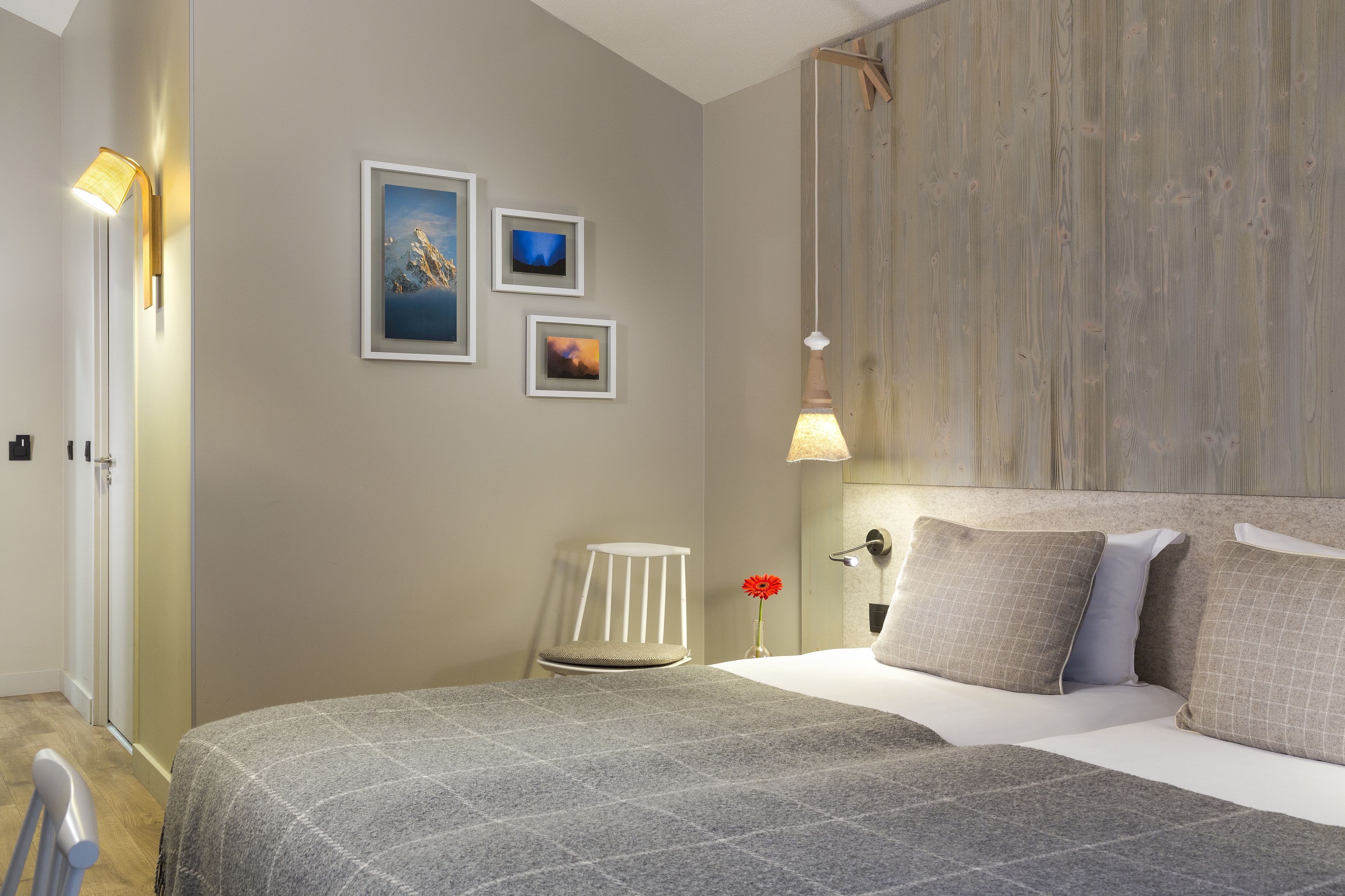 Une chambre bien rangée, avec un lit, une chaise et une table de chevet sur laquelle se trouve une lampe.