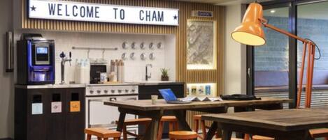 Un área de cocina moderna con un letrero que dice 'WELCOME TO CHAM', una cafetera, una estufa y una mesa de comedor con taburetes.