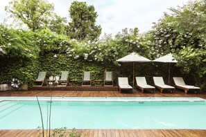 Un área de piscina con sillones y sombrillas, rodeada de abundante vegetación.