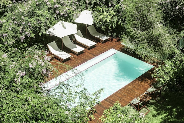 Vista aérea de una piscina rectangular rodeada de terrazas de madera y sillas de descanso blancas con sombrillas.