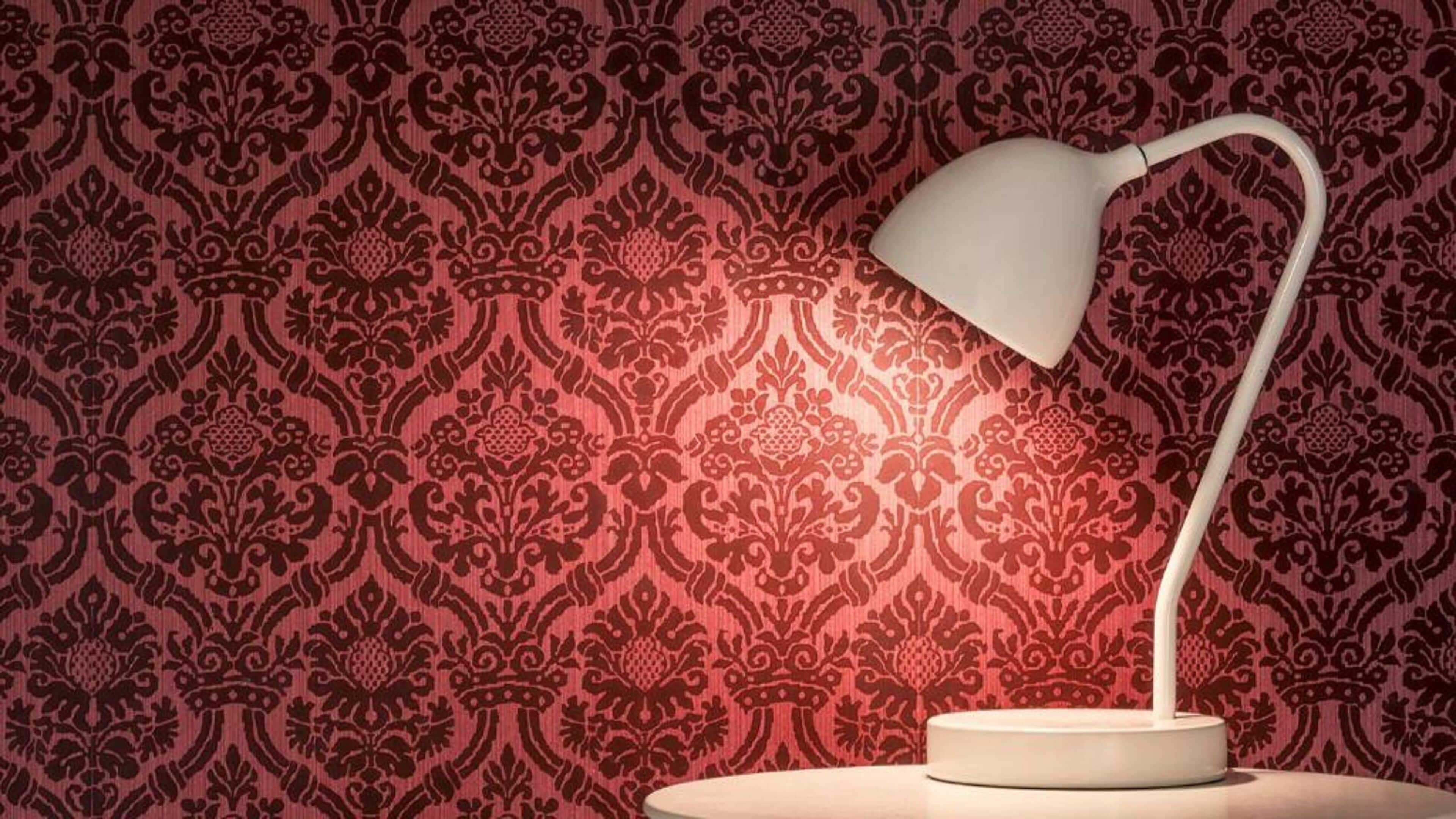 A lamp on a table against a patterned wallpaper background.