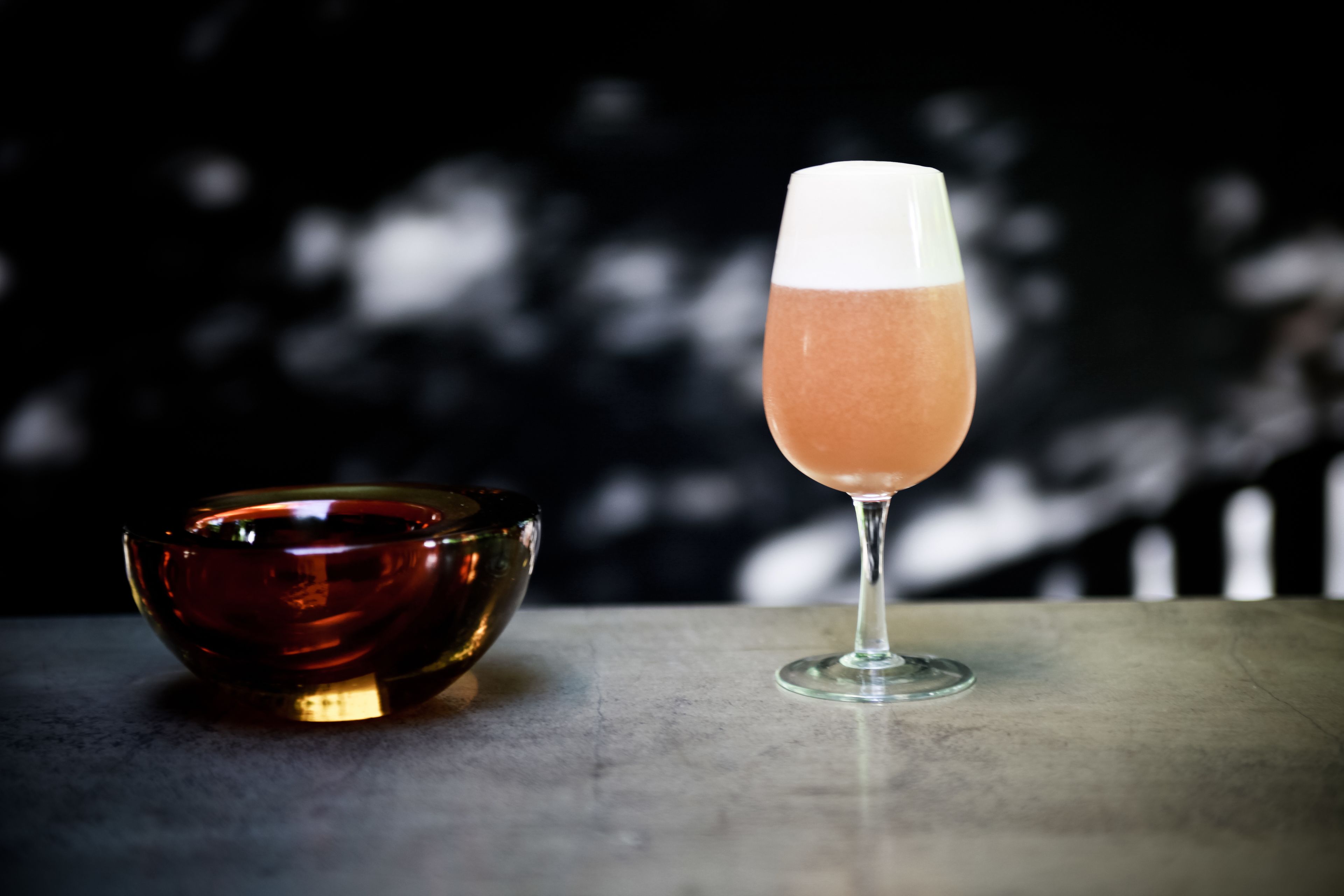 Un vaso de cóctel rosado junto a un tazón oscuro sobre una mesa.