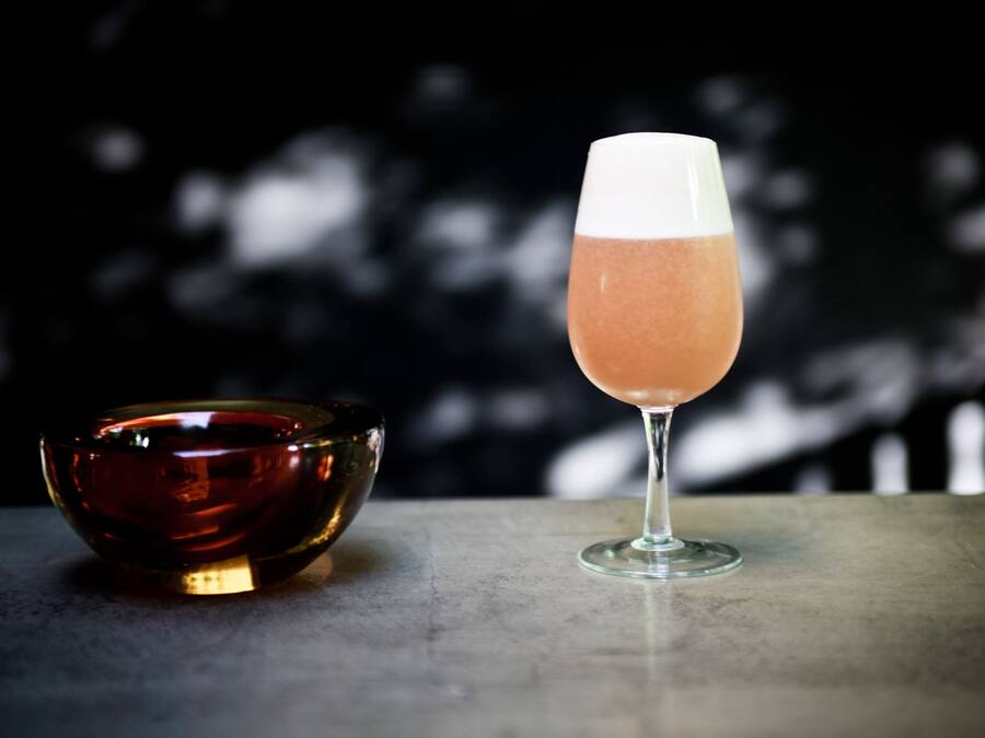 Un vaso de cóctel rosado junto a un tazón oscuro sobre una mesa.
